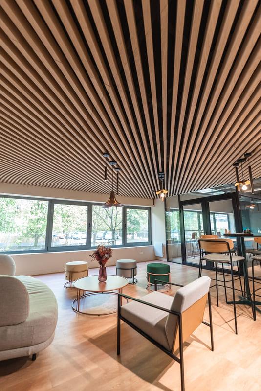 Espace détente des bureaux NECC à Marcq-en-Barœul, conçu par une architecte d’intérieur avec plafond en lames bois, mobilier design et ambiance chaleureuse propice à l’échange