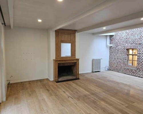 Pièce vide avec cheminée en bois au centre et mur en briques apparentes avant l'installation des meubles sur-mesure à Mouvaux