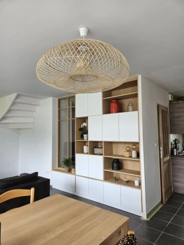meuble sur-mesure en bois et blanc séparant l’entrée du séjour avec étagères ouvertes, rangement et éléments décoratifs, apportant de la luminosité à la pièce.