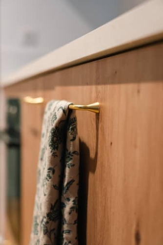 Détail sur une poignée en laiton doré sur façade bois, intégrée à un projet de rénovation cuisine par Plumbum Intérieur.