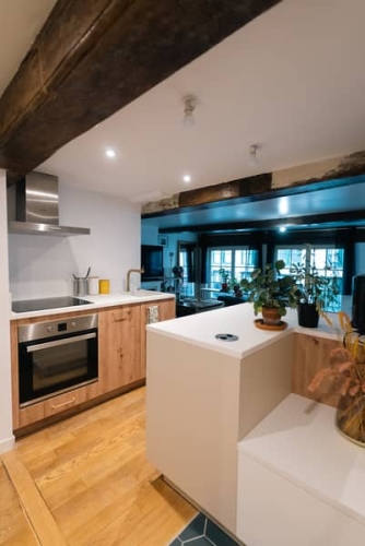 Vue globale de la cuisine ouverte rénovée, avec poutres anciennes conservées. Projet mené par une architecte d'intérieur à Lille.