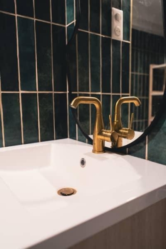 Détail d’un mitigeur doré sur plan vasque blanc dans une salle de bain design signée Plumbum Intérieur.