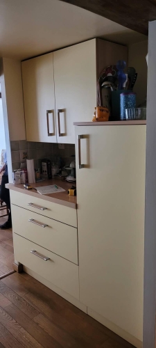 Vue de l’ancienne cuisine aux façades crème, dans un intérieur rustique avec poutres apparentes.