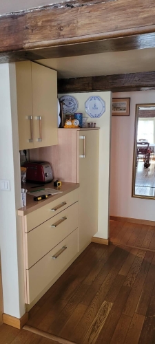 Meuble de cuisine crème avec plan de travail beige et ustensiles apparents, dans un style traditionnel.