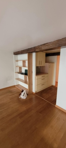 Ancienne cuisine vue depuis le séjour, avec parquet et mobilier intégré en bois clair.