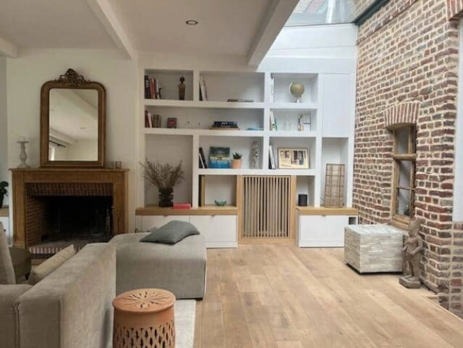 Vue d’ensemble du salon après conception de meubles sur-mesure autour d’une cheminée, avec mur en briques et puits de lumière