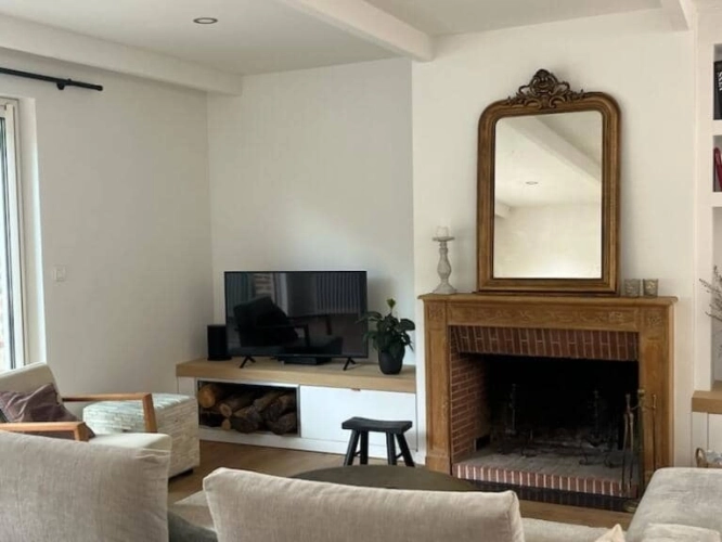 Meuble TV sur-mesure installé à gauche d’une cheminée en bois dans un salon rénové à Mouvaux